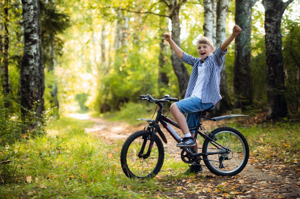 Joyful boy on a bicycle with a hands raised in the park